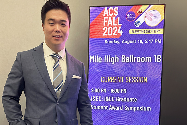 An individual stands beside a sign in a conference hall. 